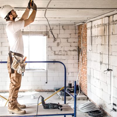 Electrician installer with a tool in his hands, working with cable on the construction site. Repair and handyman concept. House and house reconstruction.