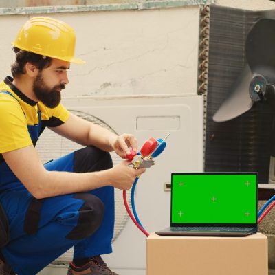 Certified technician hired by home owner to detect cause of damage to air conditioner, checking freon level values measured by professional manifold meters, displayed on chroma key laptop